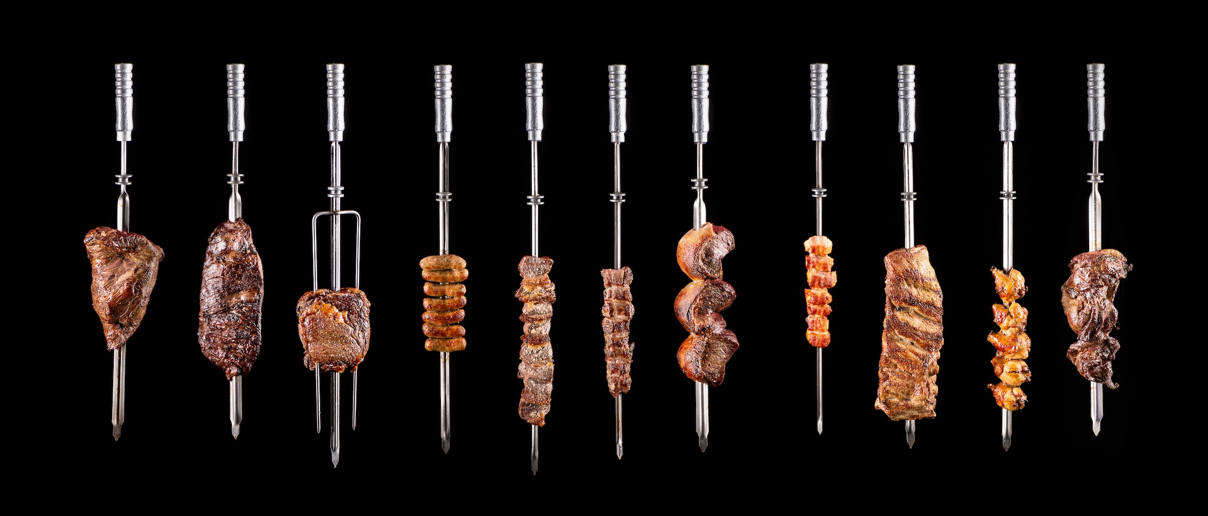 Traditional Brazilian barbecue meats on skewers on a black background